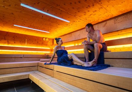 Two people are sitting in a modernly lit sauna.