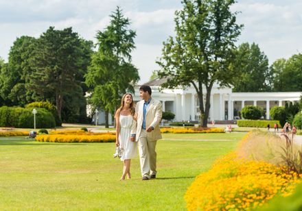 Couple on meadow in Bad Oeynhausen spa gardens with Wandelhalle