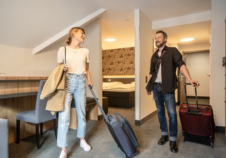 Woman and man enter hotel room with suitcases